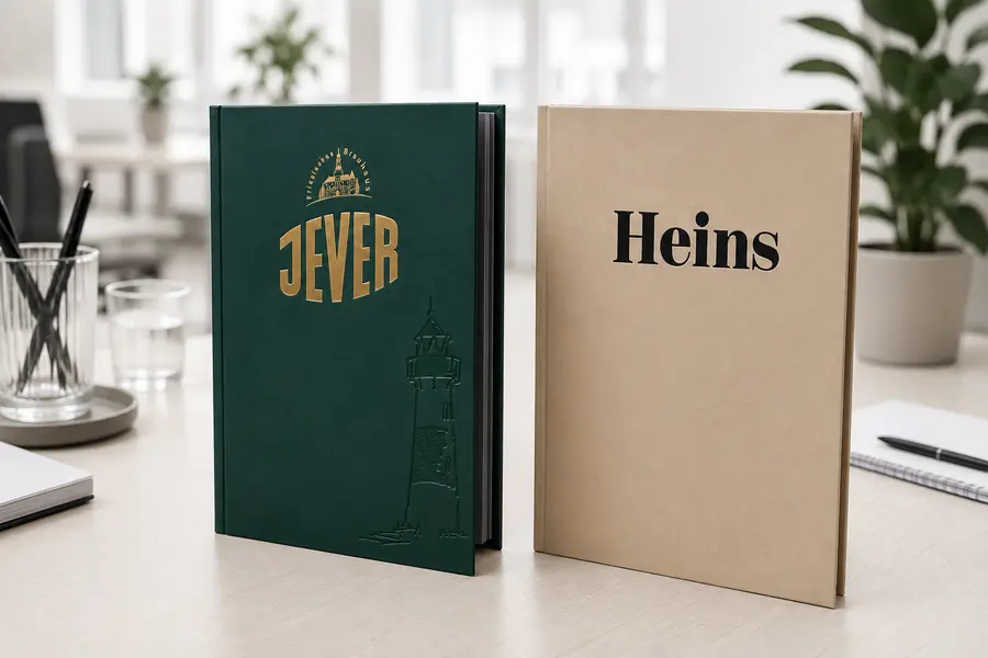 Zwei Speisekartenmappen stehend auf einem Bürotisch, links grüne Jever Kartenmappe, rechts Hellbraune Speisekartenmappe mit Heins Logo