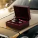 Luxuriöse Geschenkbox mit burgunderfarbenem Samtfutter auf polierter Motorhaube, goldenes Sonnenlicht beleuchtet elegantes Automobil-Geschenk