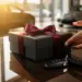 Elegante schwarze Geschenkbox mit burgunderfarbenem Band auf Autohaus-Schreibtisch, Autoschlüssel daneben, warmes Licht