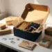 Geöffnete Influencer-Geschenkbox mit in Seidenpapier verpackten Premium-Produkten, umgeben von versiegelten Paketen mit europäischen Briefmarken auf weißem Versandtisch.