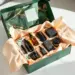 Geöffnete Premium-PR-Box in Smaragdgrün mit Goldakzenten zeigt Hautpflege, Tech-Zubehör und Luxuskerzen auf weißem Tisch