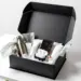 Geöffnete schwarze PR-Box mit Wasserflasche, Kaffeekapseln, Handcreme und Kopfhörern auf weißem Studiotisch