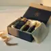 Geöffnete Premium-Geschenkbox mit in Seidenpapier eingewickelten PR-Produkten, goldenem Band und warmem Licht auf weißer Fläche.