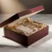 Luxuriöse Influencer-Unboxing-Box in Burgunderrot und Mattgold, halb geöffnet mit Seidenpapier und kuratierten Produkten auf Marmor.