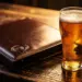 Aufgeklappte Leder-Speisekarte auf rustikalem Holztisch neben einem beschlagenen Bierglas im warmen Kerzenlicht.