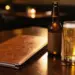 Aufgeschlagene Leder-Menümappe auf poliertem Restauranttisch neben einer Craft-Beer-Flasche und einem Glas goldenem Lager im Kerzenlicht.