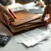 Personalisierte Lederordner mit Prägung auf weißem Schreibtisch, Taschenrechner und Rechnungen, Hände beim Organisieren