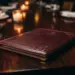 Aufgeschlagene Ledermappe auf poliertem Eichentisch in elegantem Restaurant, warmes Kerzenlicht beleuchtet burgunderrote Oberfläche.