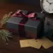 Luxuriöse Geschenkbox mit burgunderroter Schleife, Tannenzweigen und goldenen Geschenkanhängern auf dunklem Walnussholz.