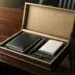 Offene Executive-Onboarding-Box mit Leder-Notizbuch, Markenstift und Karte auf dunklem Walnussholz-Schreibtisch mit goldenen Akzenten.