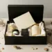 Offene matte Geschenkbox in Schwarz mit Produktproben, handgeschriebenem Brief auf Cremepapier und getrockneten Botanicals in Gold- und Elfenbeintönen.