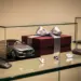 Elegante Geschenkbox mit Schleife neben Luxusauto-Miniatur in Autohaus-Vitrine mit Lederaccessoires und warmem Licht