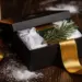 Geöffnete matte schwarze Geschenkbox mit Premium-Firmengeschenken, Tannenzweig und Goldband auf dunkler Walnussoberfläche mit Schnee.