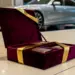 Luxuriöse burgunderfarbene Samtgeschenkbox mit goldener Schleife steht geöffnet im Autohaus-Showroom