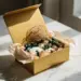 Geöffnete Luxus-Geschenkbox auf Marmor mit in Seidenpapier gewickelten Produktproben und getrockneten Botanicals in Gold-, Creme- und Waldgrüntönen.