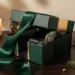 Luxuriöse Geschenkbox mit Satinband, halb geöffnet, auf dunklem Walnussholz mit Tannenzweigen und goldenen Weihnachtskugeln.