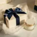 Luxuriöse Geschenkbox mit Satinband und Seidenpapier neben einem Premium-Kosmetikprodukt auf Marmoroberfläche in Gold- und Marineblautönen.