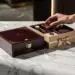 Luxuriöse Mahagoni-Geschenkbox mit Goldfolie neben schlichter Kraftpapier-Box auf poliertem Marmor im eleganten Showroom