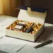 Geöffnete Luxus-Geschenkbox mit Produktmustern in Seidenpapier, umgeben von Planungsnotizen und Stift auf weißem Schreibtisch.