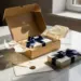 Geöffnete Luxus-Geschenkbox mit Seidenpapier, versiegeltem Umschlag und schleifenverpacktem Produkt auf Marmoroberfläche in Creme, Navy und Gold.