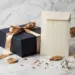 Luxuriöse Geschenkbox mit Satinband und versiegeltem Versandumschlag auf Marmor, umgeben von getrockneten Botanicals in Navy, Gold und Elfenbein.