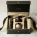 Geöffnete Influencer-Unboxing-Geschenkbox aus mattem Schwarz mit Goldfolienakzenten auf Marmoroberfläche, gefüllt mit Kosmetikprodukten und Seidenpapier.