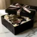 Luxuriöse Influencer-Unboxing-Geschenkbox aus mattem Schwarz mit Satinband, Glasparfümflakon und Seidenpapier auf weißem Marmor.