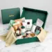 Luxuriöse smaragdgrüne PR-Box mit Goldprägung enthält Tech-Zubehör, Wellness-Produkte und Gourmet-Snacks auf Marmortisch