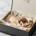 Geöffnete PR-Box mit Glasflakon, Seidenband und Seidenpapier auf weißem Marmor in Gold- und Elfenbeintönen.