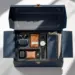 Offene marineblaue PR-Box mit goldenen Akzenten enthält Kopfhörer, Smartwatch, Kaffeekapseln und Notizbuch auf weißem Tisch