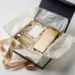 Geöffnete Luxus-Geschenkbox mit Premium-Produktproben, Seidenpapier und Markeninserts in Champagner- und Elfenbeintönen auf weißem Untergrund.