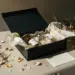 Geöffnete matte Luxus-Geschenkbox mit Produktproben in Seidenpapier, handgeschriebenem Kärtchen und getrockneten Botanicals in Gold- und Elfenbeintönen.