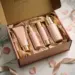 Geöffnete Influencer-Unboxing-Box mit in Seidenpapier verpackten Premiumprodukten, Rosenblättern und Goldband auf weißem Marmor.