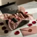 Geöffnete Influencer-Unboxing-Box auf Marmor mit Seidenpapier, Kosmetikproben, Rosenblättern und versiegeltem Umschlag in Schwarz, Rosé und Gold.