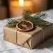 Nachhaltiges Weihnachtsgeschenk in Kraftpapier-Box mit Tannenzweigen und getrockneten Orangenscheiben auf weißem Leinenstoff.