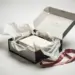 Geöffnete Onboarding-Geschenkbox mit zerknittertem Band und verschobenen Inhalten auf weißer Oberfläche.