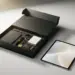 Matte schwarze Onboarding-Geschenkbox mit geöffnetem Deckel neben Tablet mit Willkommensbildschirm auf weißem Schreibtisch.