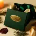 Personalisierte Geschenkbox in Dunkelgrün mit goldenem Namensprägung, Satinband und Tannenzweigen im warmen Kerzenlicht.
