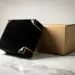 Matte schwarze Premiumverpackung mit Goldfolien-Akzenten neben einer Kraftkarton-Box auf weißem Marmor, warmes Studiolicht.