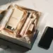 Geöffnete Premium-Geschenkbox mit eingewickelten Kosmetikprodukten, Seidenband und Seidenpapier auf Marmor neben einem Smartphone.