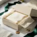 Geöffnete Premium-Geschenkbox in Creme und Dunkelgrün mit goldenen Akzenten, seidenpapier und Verpackungsmaterial auf weißem Marmor.