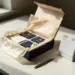 Premium-Geschenkbox mit Seidenpapier und Produktproben auf weißem Schreibtisch, Kalender und Stift daneben, warme Elfenbein- und Marineblauntöne mit Goldakzenten.