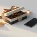 Elegante Geschenkbox mit Satinband auf weißer Oberfläche, daneben Smartphone mit Lifestyle-Foto, warmes Champagnerlicht.