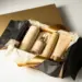 Geöffnete Premium-Geschenkbox mit in Seidenpapier eingewickelten Produkten, goldenen und elfenbeinfarbenen Verpackungsmaterialien auf weißem Untergrund.