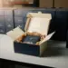 Gestapelte Premium-Geschenkboxen in Navy, Creme und Gold auf einem Versandtisch, eine geöffnet mit Seidenpapier und Luxusverpackung.