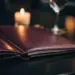 Aufgeschlagene Leder-Menümappe auf dunklem Restauranttisch mit Kerze und Weinglas im unscharfen Hintergrund.