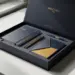 Geöffnete Premium-Onboarding-Box mit Notizbuch, Markenstift und Willkommenskarte in Navy und Gold auf weißem Schreibtisch.