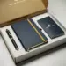 Geöffnete Onboarding-Box mit Notizbuch, Stift und Willkommenskarte in Navy und Gold auf weißem Untergrund.
