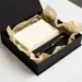 Matte schwarze Onboarding-Box mit Willkommenskarte, Stift und Seidenpapier auf weißem Schreibtisch, Studiobeleuchtung.