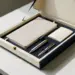 Geöffnete Premium-Onboarding-Box mit Notizbuch, Stift und Willkomenskarte in Creme und Marineblau mit Goldakzenten auf weißem Schreibtisch.